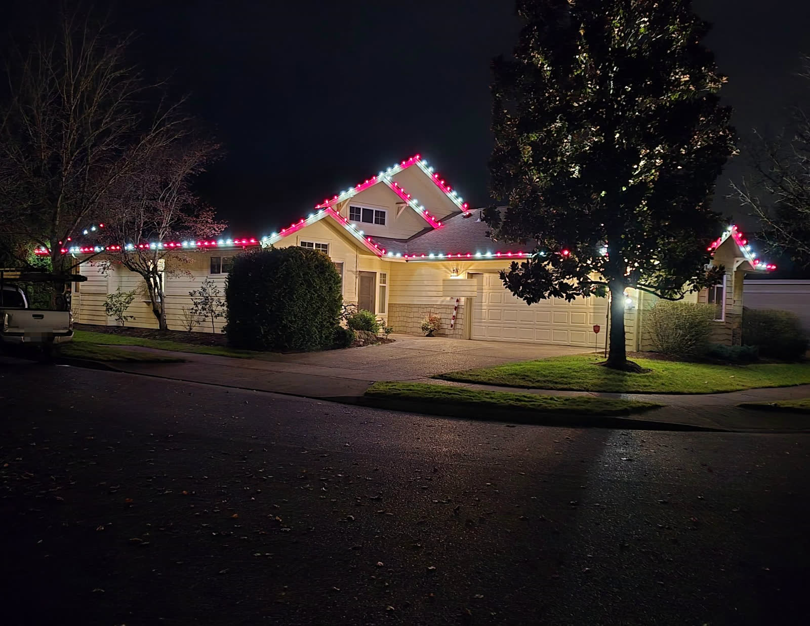 Holiday lights outlining a roofline at night in red and white, with the crew truck parked at the curb