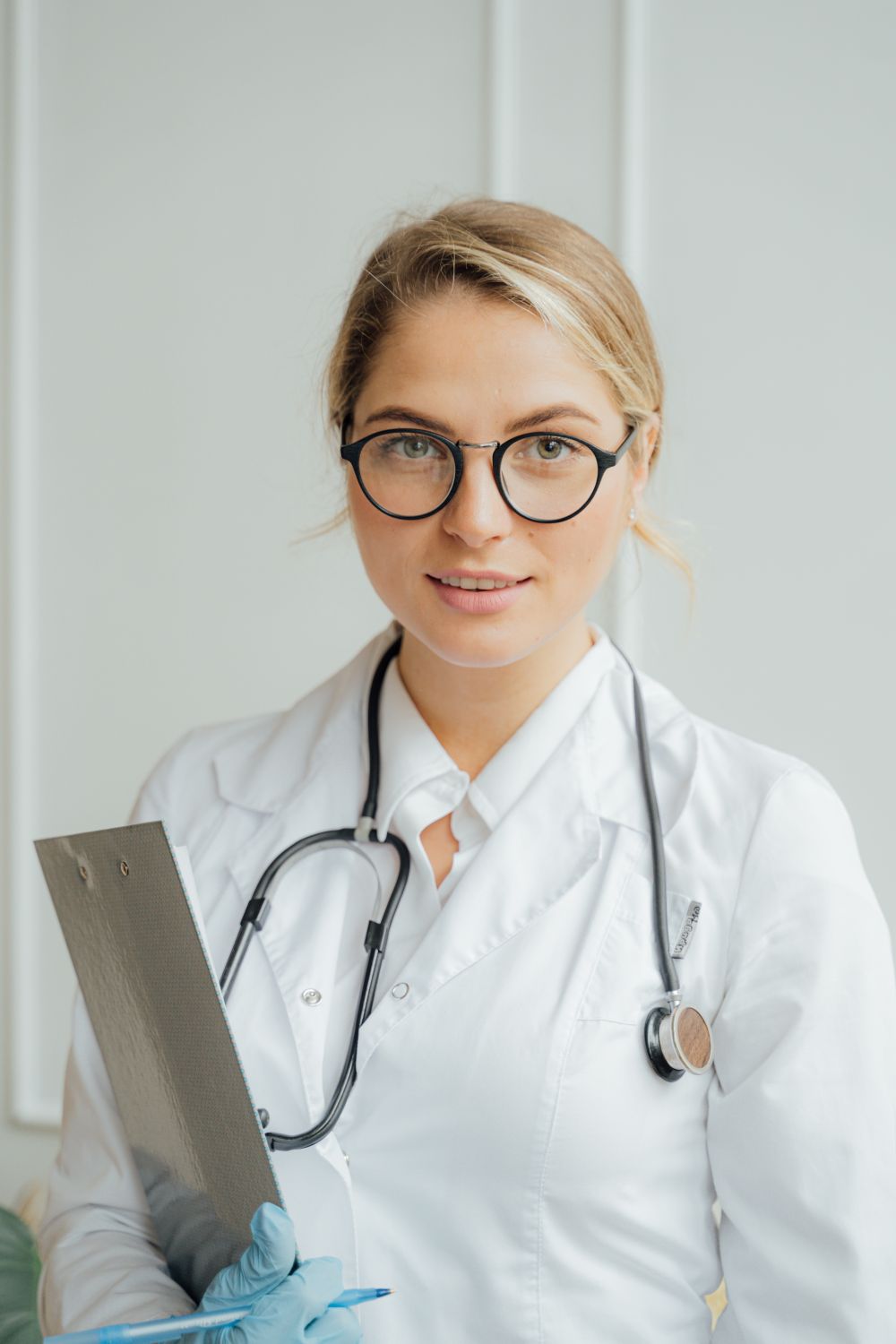 A healthcare professional in a white coat holding a clipboard — the documentation layer every requirement eventually lands on
