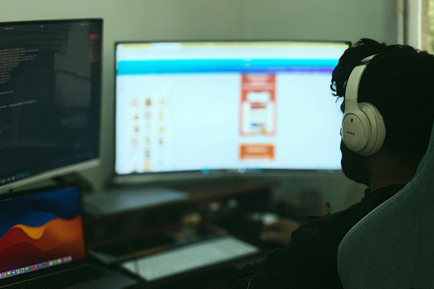 A developer in silhouette at a desk, lit only by an ultrawide monitor and a laptop, a code editor open beside them